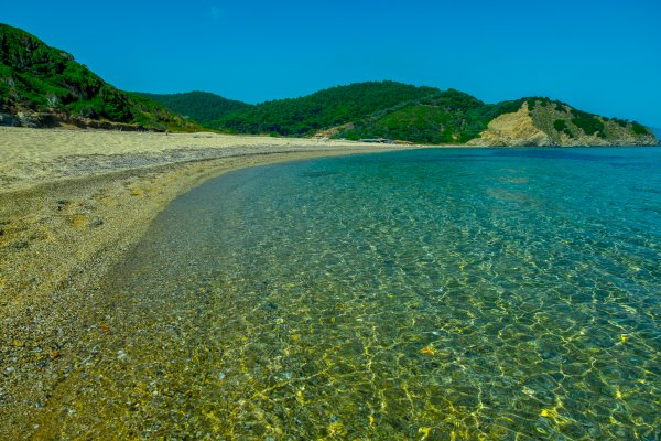 A green-blue picture with waters, the Megalos Aselinos Beach on Skiathos, and hills.