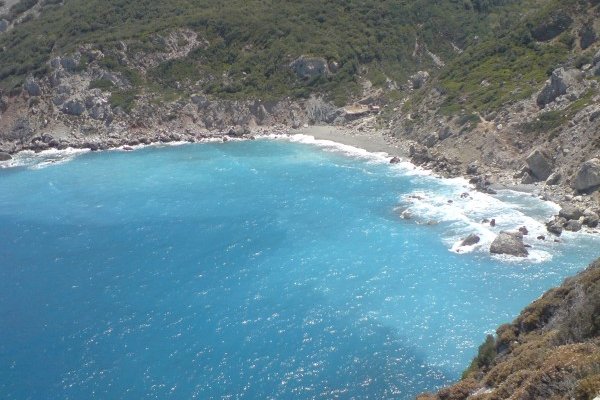 A bay with turquoise waters breaking on rocks and a sandy beach on Megas Gialos, Skiathos.