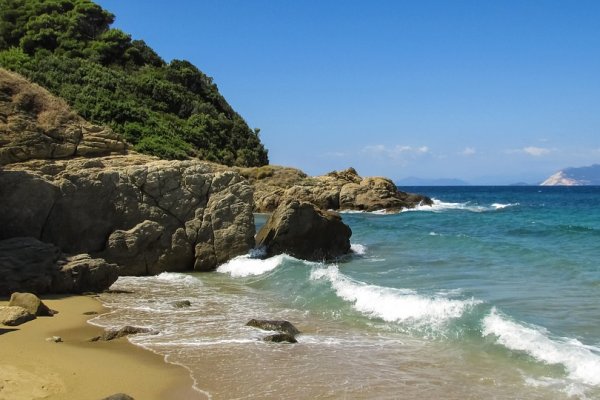 Waves pounding the rocks and a piece of Small Banana beach' sand at the foot of a green hill in Skiathos. 