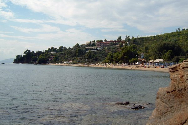 A distant picture of Troulos Beach at the foot of a green hill with a few houses.