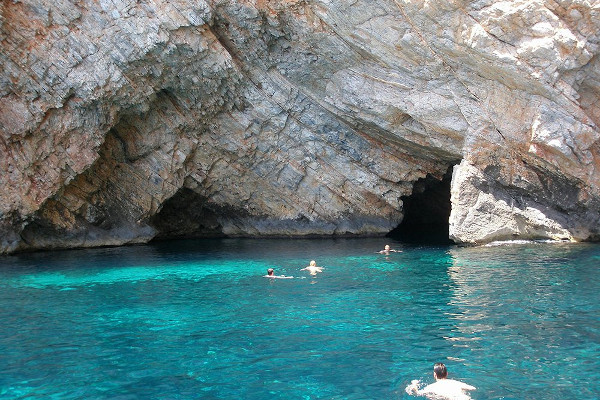 People swimming in the crystal clear waters in front of the Pentekali & Diatripti Sea Caves at Skyros Island.