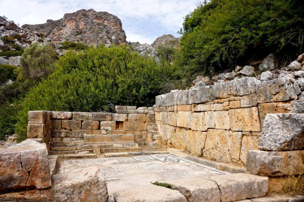 Ruins and a mosaic, and in the background trees and humongous rock at the Archaeological Site of Ancient Lissos, Sougia.