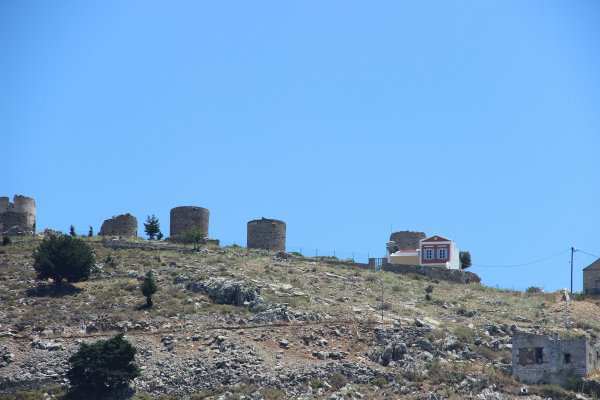 An arid hill with five mills without blades, one of them visibly damaged, in Symi.