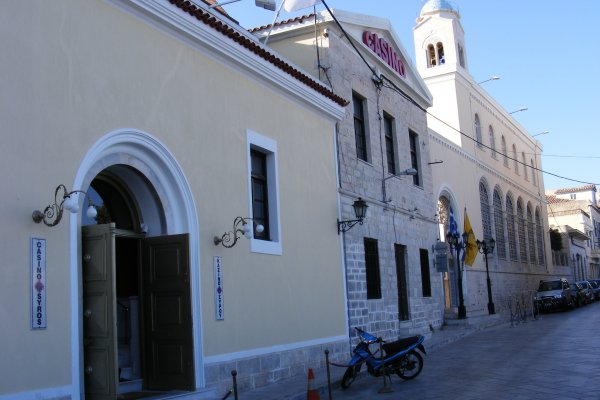 A street with white buildings and a parked motorbike in front of Casino Syros.
