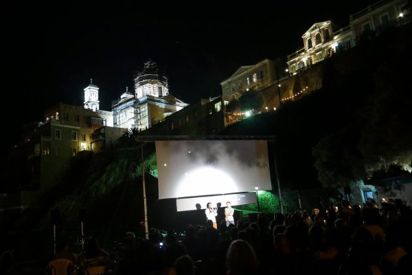 An open air screening at night below a lit church and other buildings.