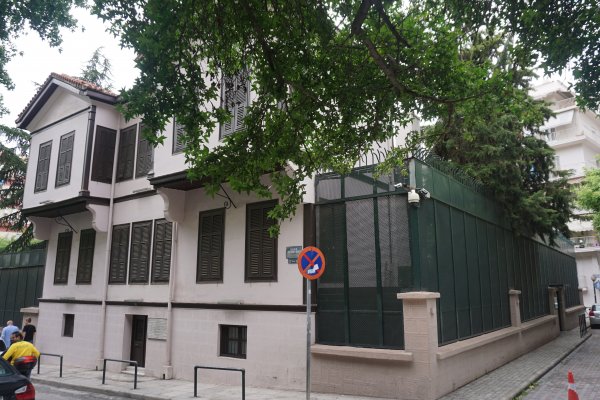 A house of old Macedonian architecture with closed windows framed below a tree branch.