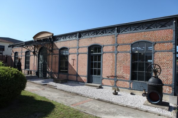 A brick-built building with black steel pillars and an old water pump part in the front.