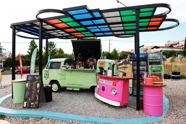 Colorful truck parts made into a bar and restaurant under a colorful shelter and all that on gravel.