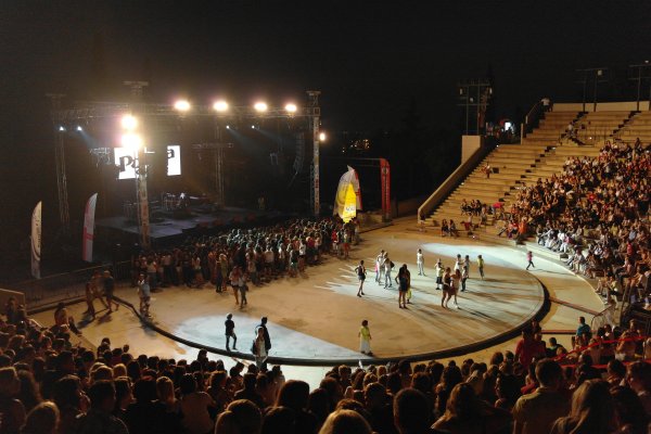 A half-full amphitheater with a choir and children on a lit stage during night.